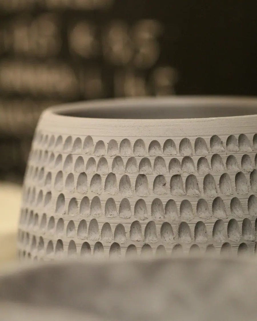Detalhe de um vaso de cerâmica clara com relevo.